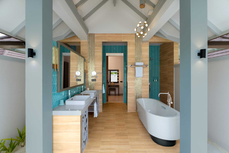 A suite bathroom at Sun Siyam Olhuveli with turquoise tiling, twin basins and a freestanding bath.