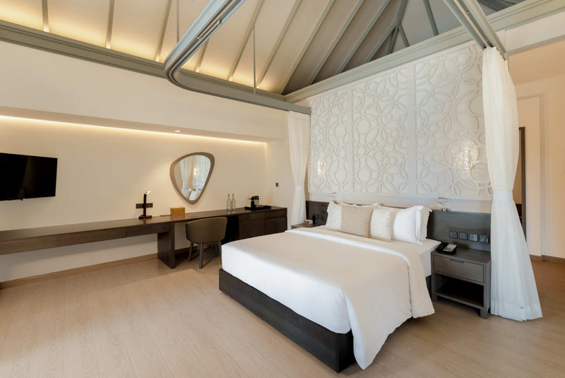 A suite bedroom at Sun Siyam Olhuveli with drapes at the bedhead, a desk and a television.