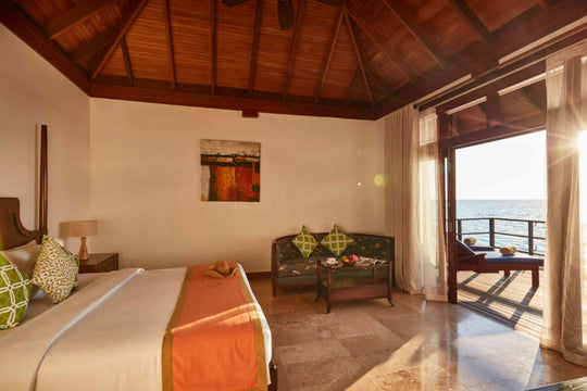 Sun Siyam Olhuveli, South Malé Atoll — Deluxe Water Villa bedroom with the doors open to the lagoon
