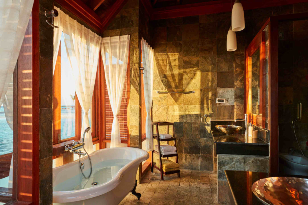 Sun Siyam Olhuveli, South Malé Atoll — stone and timber bathroom with a freestanding bath beside the lagoon windows