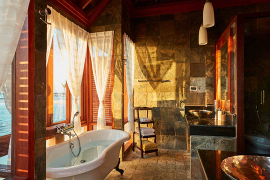 Sun Siyam Olhuveli, South Malé Atoll — stone and timber bathroom with a freestanding bath beside the lagoon windows