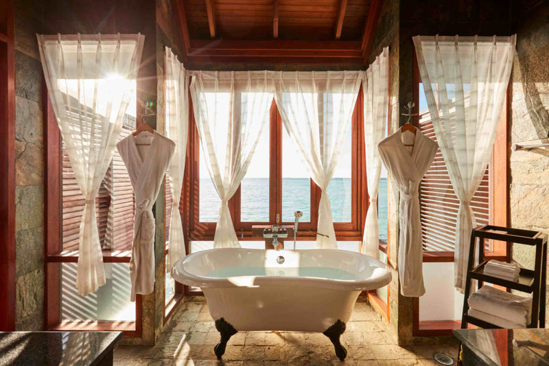 A clawfoot bath at Sun Siyam Olhuveli in front of shuttered windows over the water.