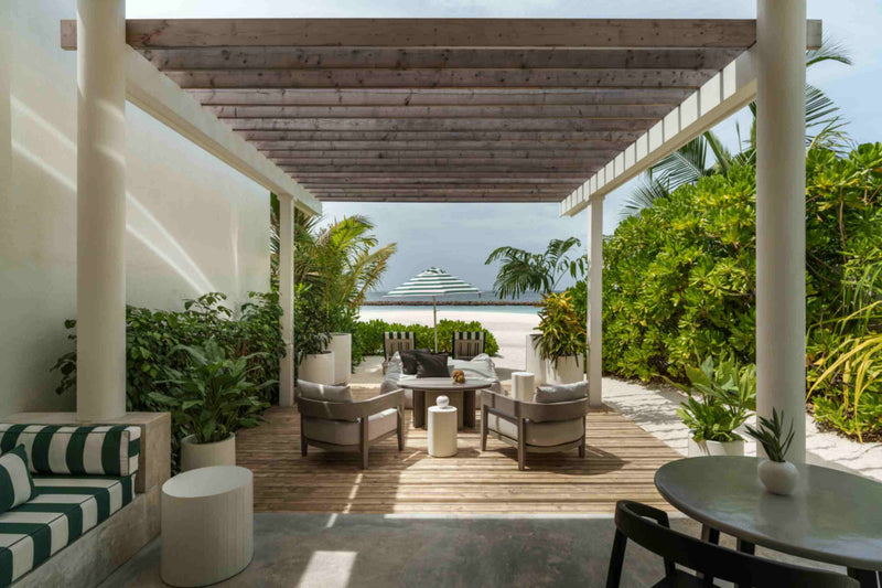 A covered terrace at Sun Siyam Iru Veli under a timber pergola, armchairs around a low table, looking out through planting to the sea.