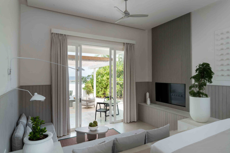 A living area at Sun Siyam Iru Veli with a sofa facing sliding doors onto a covered terrace, a wall-mounted television and a planter.