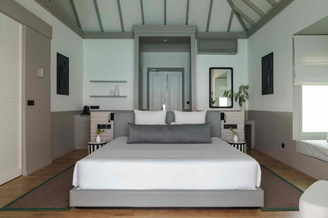 Sun Siyam Iru Veli, Dhaalu Atoll — bedroom under a vaulted ceiling with dark beams, looking through to the terrace and the sea