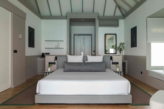 Sun Siyam Iru Veli, Dhaalu Atoll — bedroom under a vaulted ceiling with dark beams, looking through to the terrace and the sea