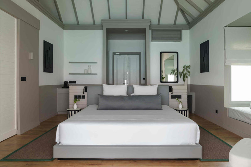 A bedroom at Sun Siyam Iru Veli under a vaulted ceiling with dark beams, looking through to the terrace and the sea.