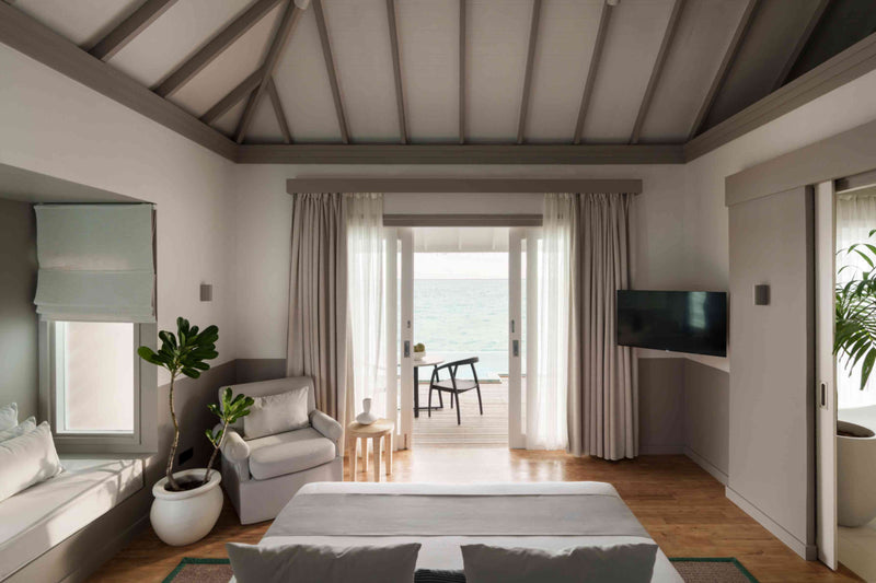 A bedroom at Sun Siyam Iru Veli looking out through open doors to the deck and the sea.