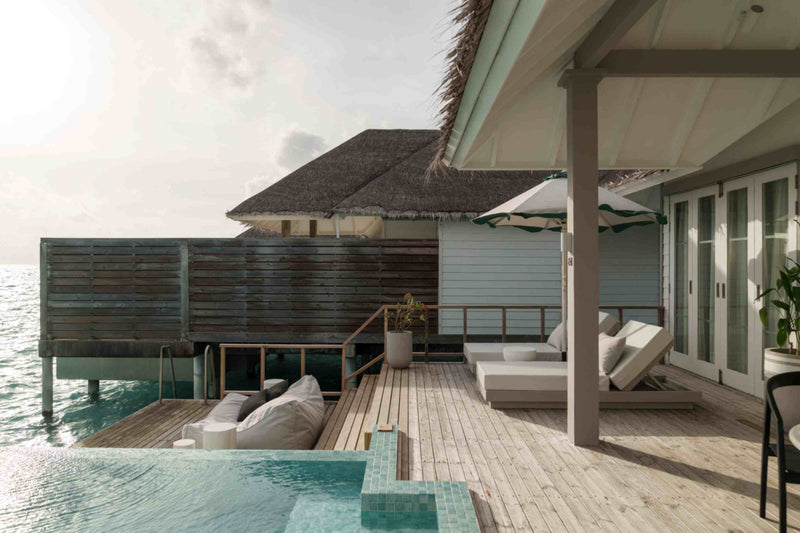 An overwater villa exterior at Sun Siyam Iru Veli, thatched roof over a deck with a daybed and pool.