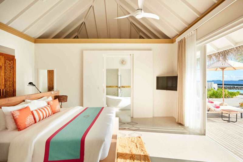 A bedroom at Sun Siyam Iru Veli under a vaulted ceiling with a fan, the ensuite, and doors to a deck.