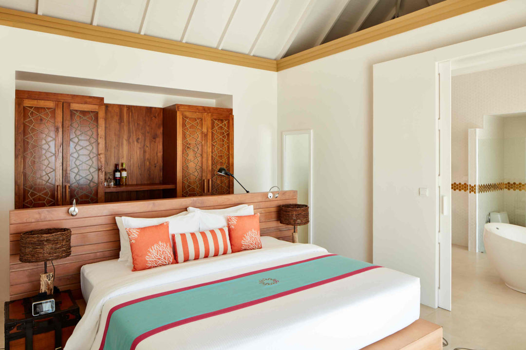 Sun Siyam Iru Veli, Dhaalu Atoll — bedroom with a carved timber wardrobe wall and a coral and teal bed runner
