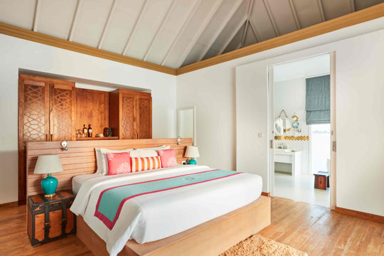 Sun Siyam Iru Veli, Dhaalu Atoll — bedroom with a carved timber wall and bar cabinet, ensuite beyond