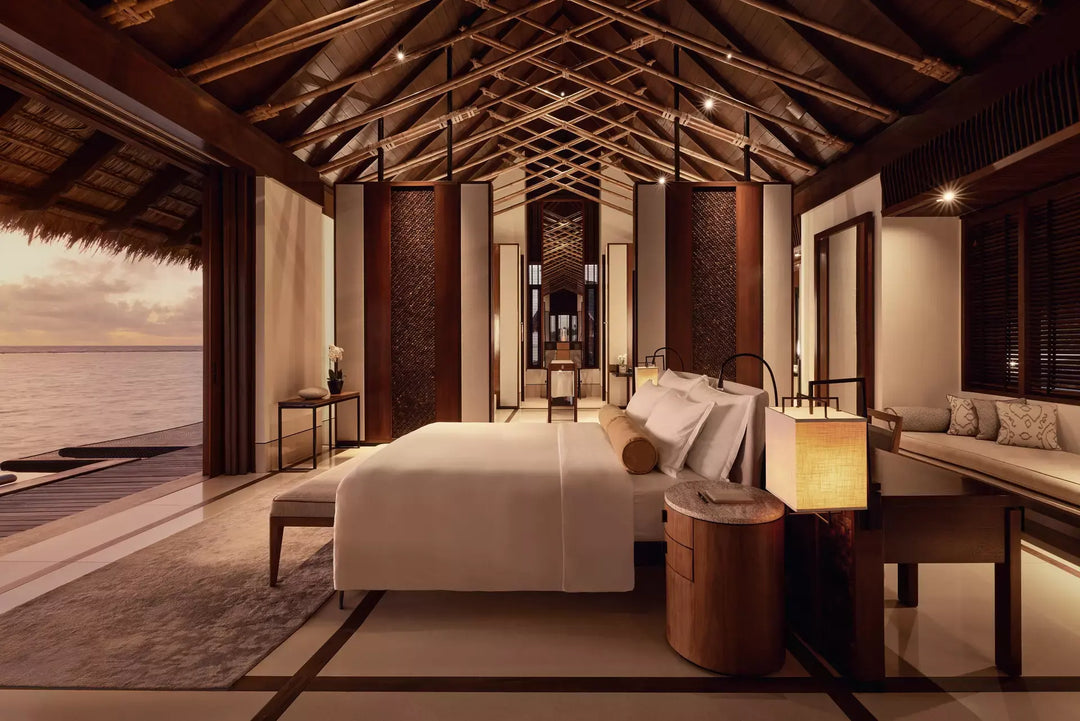 One&amp;Only Reethi Rah Water Villa with Pool at dusk, lamps lit beside the bed and the doors open to the lagoon
