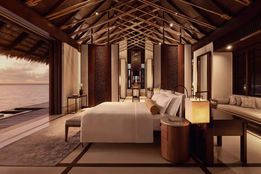 One&Only Reethi Rah Water Villa with Pool at dusk, lamps lit beside the bed and the doors open to the lagoon