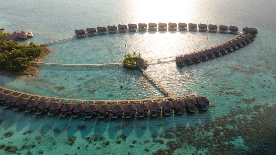 The overwater villas at Ayada Maldives from the air with the sun on the water behind them