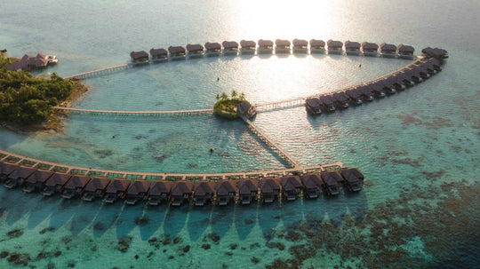 The overwater villas at Ayada Maldives from the air with the sun on the water behind them