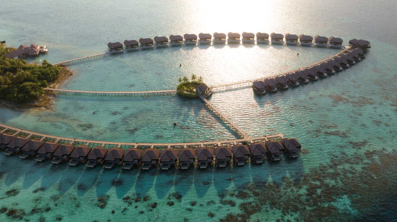 The overwater villas at Ayada Maldives from the air with the sun on the water behind them