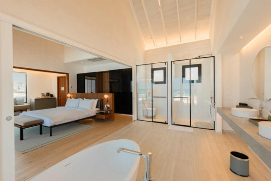 A bedroom at ananea Madivaru Maldives with the glass-walled bathroom behind the bed