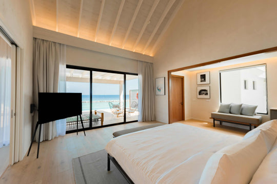 A bedroom at ananea Madivaru Maldives looking past the television to the deck and the sea beyond