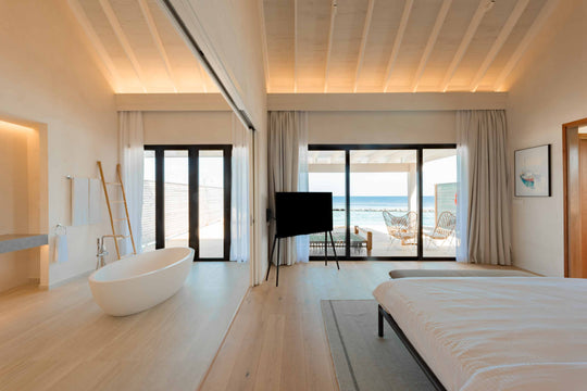 A villa interior at ananea Madivaru Maldives, freestanding bath beside the bed with doors open to the deck