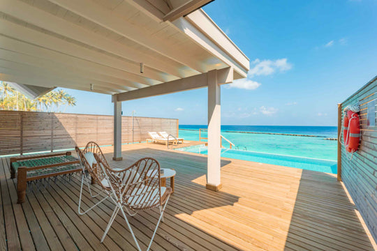 The shaded deck of an overwater villa at ananea Madivaru Maldives, rattan chairs beside the private pool with the lagoon beyond