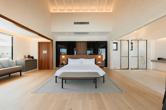A villa bedroom at ananea Madivaru Maldives seen from the sitting area, the bed centred between glazed screens