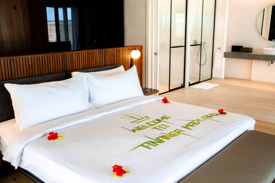 A bed at ananea Madivaru Maldives made up with a welcome message written in palm leaves and red flowers