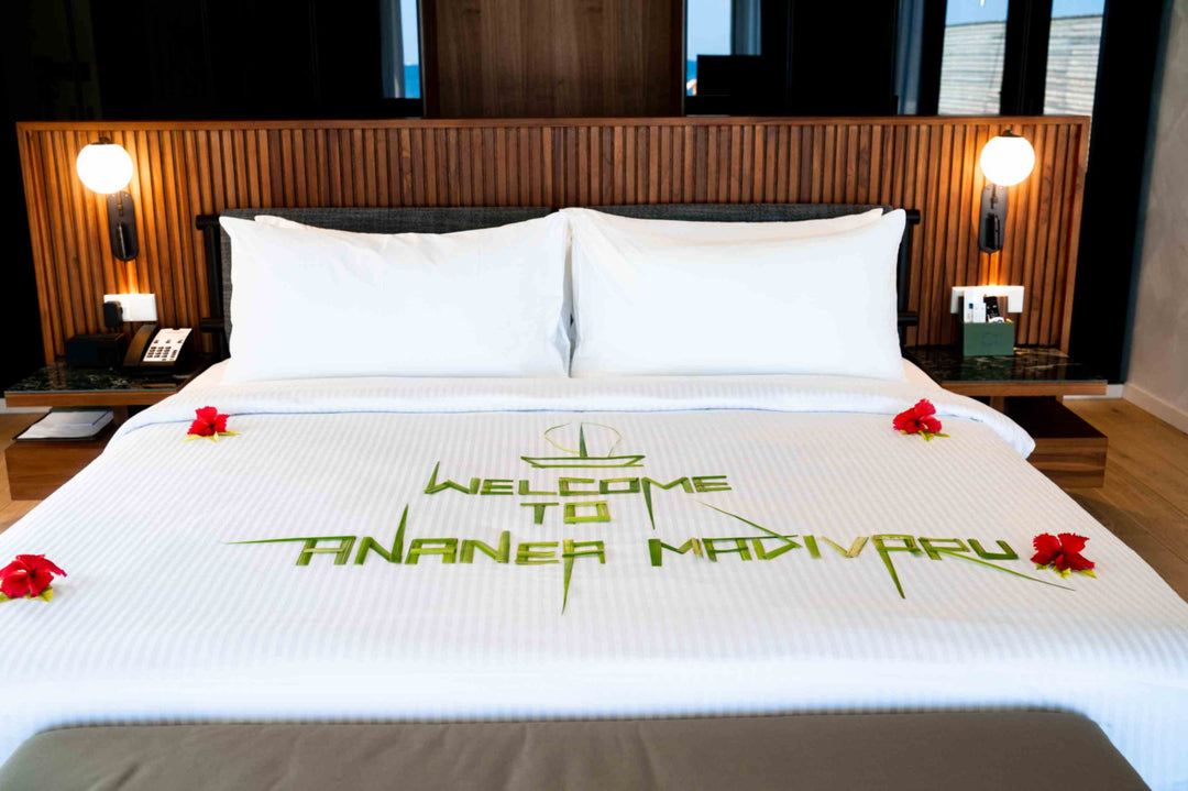 A welcome message to ananea Madivaru Maldives laid out in palm leaves and red flowers across the bed