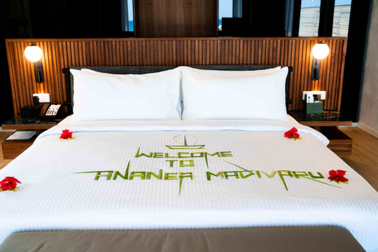 A welcome message to ananea Madivaru Maldives laid out in palm leaves and red flowers across the bed