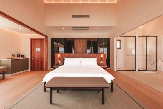 A villa bedroom at ananea Madivaru Maldives, the bed against a timber headboard wall between two glazed shower screens