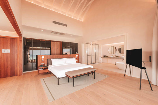 A villa bedroom at ananea Madivaru Maldives with a television on a stand and the glazed bathroom behind