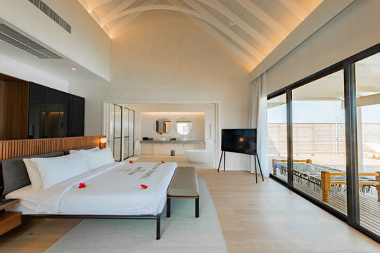 A villa bedroom at ananea Madivaru Maldives dressed with red flower petals, the bathroom and deck beyond