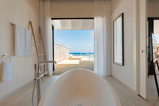 A villa bathroom at ananea Madivaru Maldives looking past the bath and out to the deck and the sea