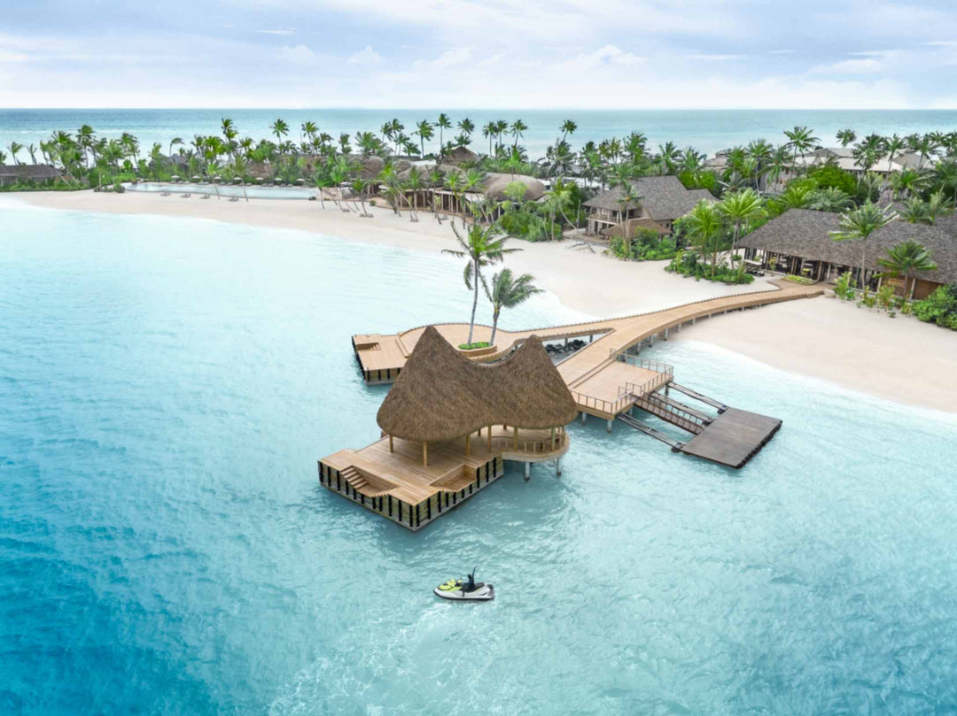 The thatched overwater pavilion at ananea Madivaru Maldives from the air, a jetty linking it to the beach and a boat alongside