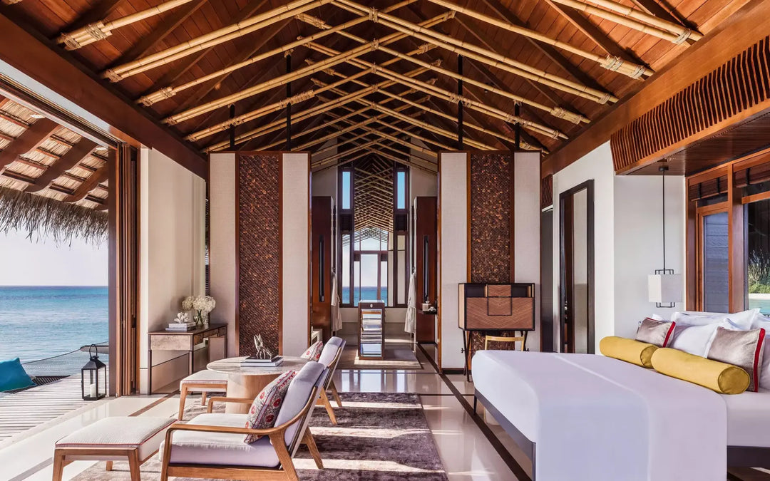 One&amp;Only Reethi Rah Water Villa interior, the bed and seating area open to the deck and lagoon through folding doors