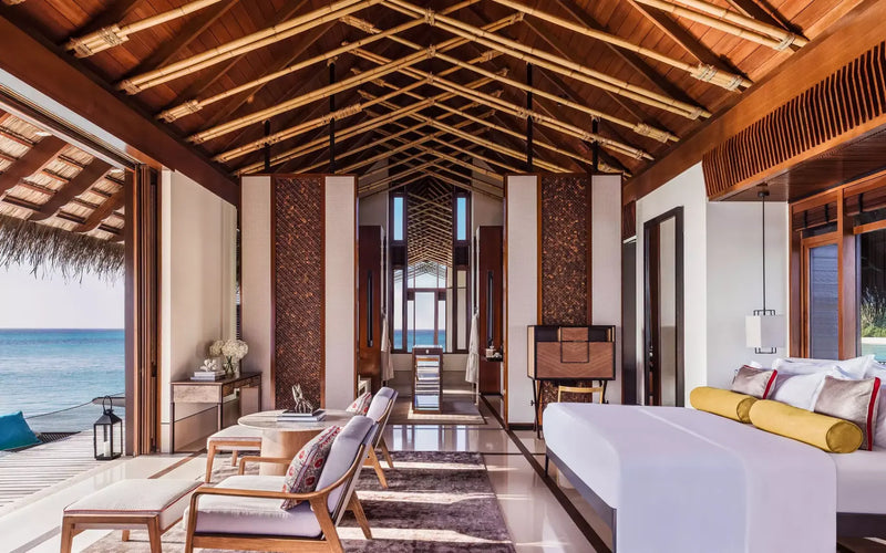 One&Only Reethi Rah Water Villa interior, the bed and seating area open to the deck and lagoon through folding doors