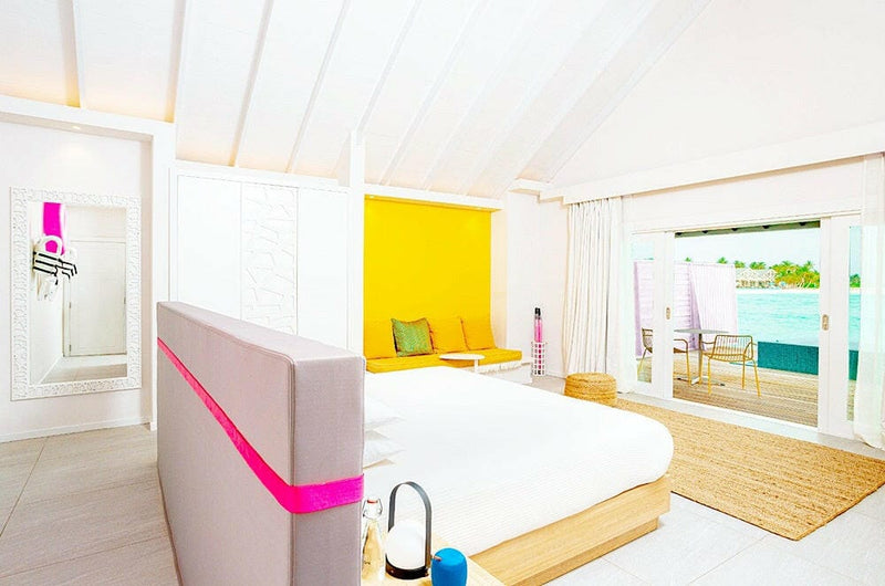 A villa bedroom at The Standard Huruvalhi, a pink stripe across the bed base with a yellow wall behind.