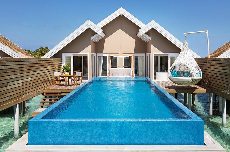 A water villa deck at LUX* South Ari Atoll, long blue pool and a hanging white egg chair.