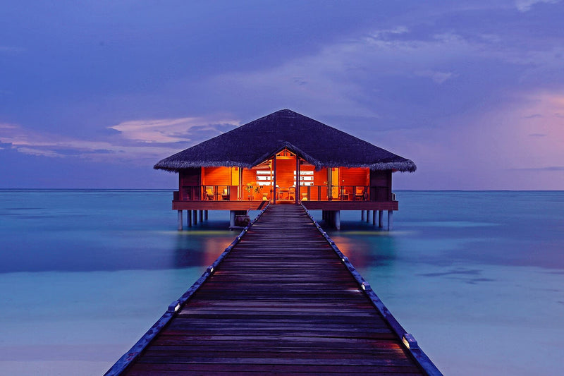 The overwater spa lit at dusk at the end of its jetty, Medhufushi Island Resort
