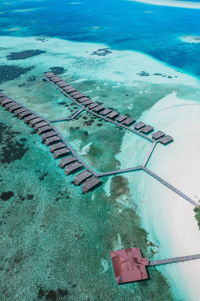 Water villas on their jetty over the wide shallow lagoon at Medhufushi, seen from the air