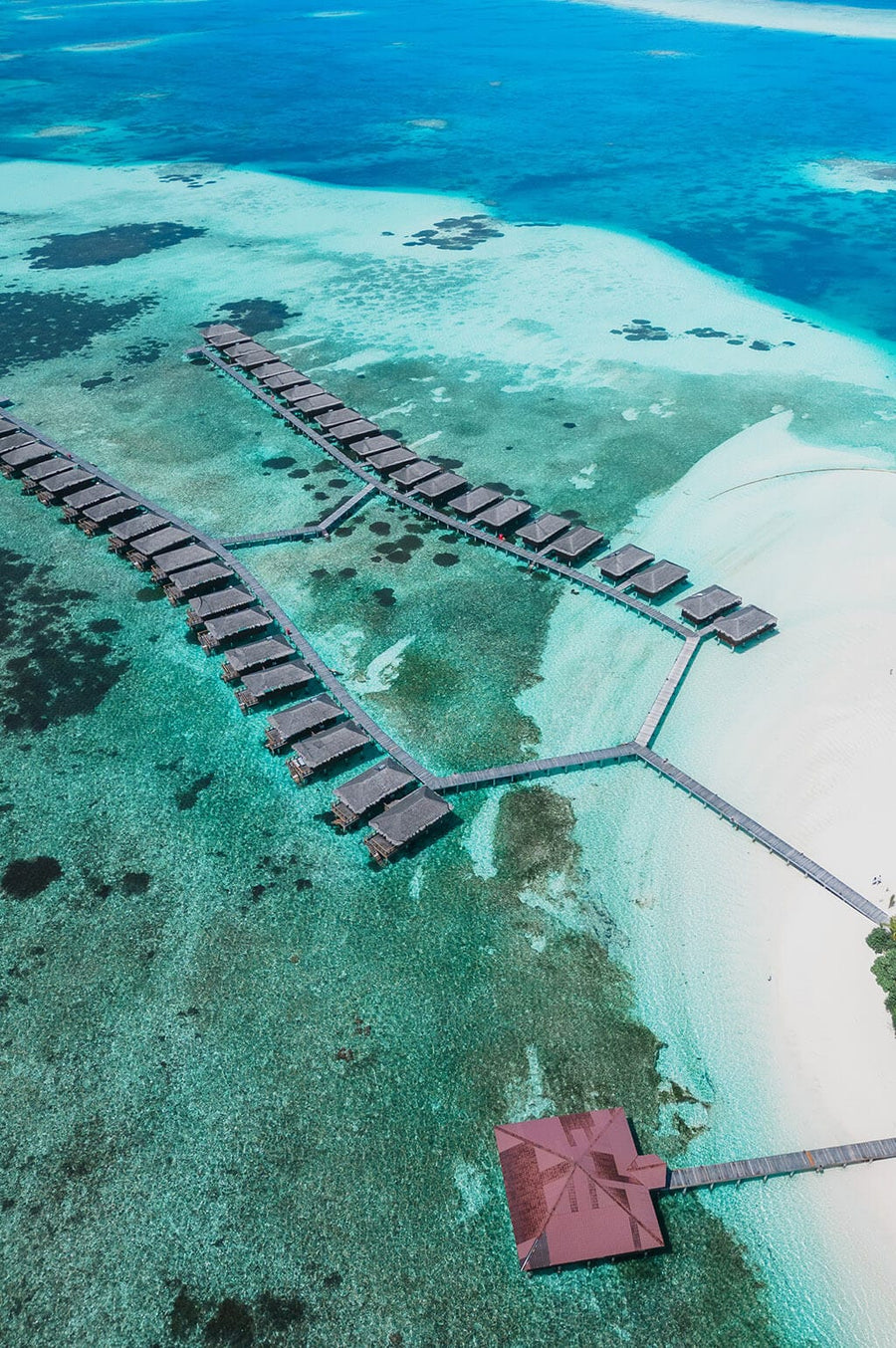 Water villas on their jetty over the wide shallow lagoon at Medhufushi, seen from the air