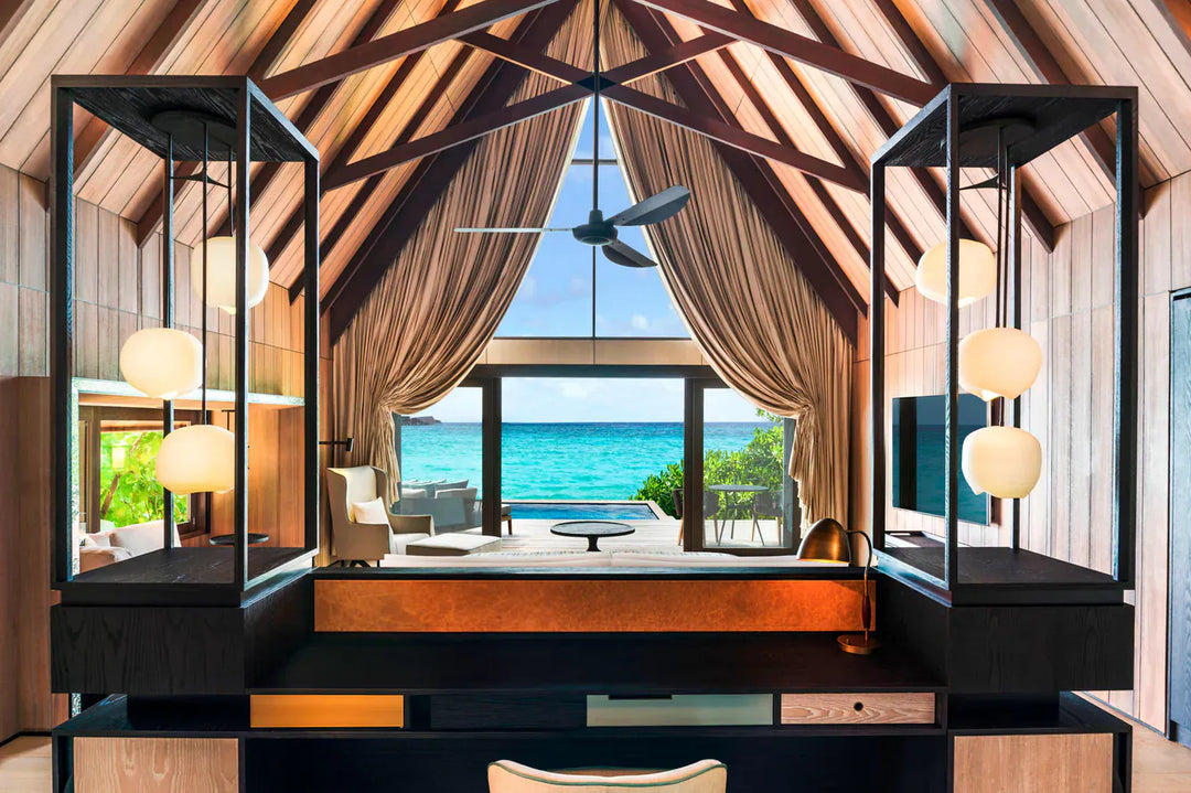 The St. Regis Maldives Vommuli, Dhaalu Atoll — Bedroom under a vaulted timber ceiling, the bed facing open doors onto a deck and the lagoon