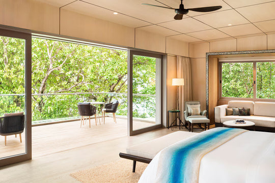 The St. Regis Maldives Vommuli, Dhaalu Atoll — Bedroom with a king bed and sliding glass onto a deck with loungers, greenery beyond