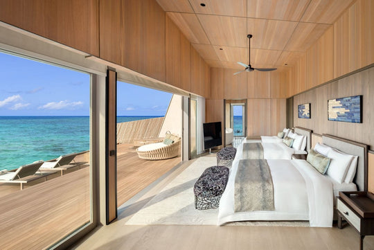 The St. Regis Maldives Vommuli, Dhaalu Atoll — Timber-lined bedroom with a king bed and a glass wall onto a deck above the water