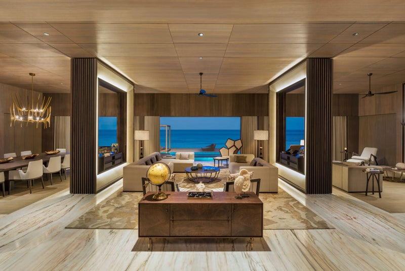 A living room at The St. Regis Maldives Vommuli with pale timber floors and sea views on two sides, dining area beyond.