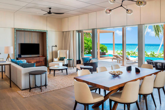 The St. Regis Maldives Vommuli, Dhaalu Atoll — Open-plan living and dining room with glass doors onto a deck above the lagoon