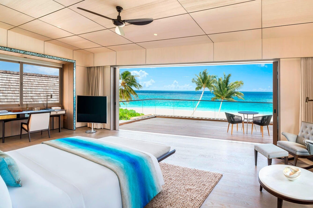 The St. Regis Maldives Vommuli, Dhaalu Atoll — Bedroom opening onto a deck and the beach, with seating and palms outside