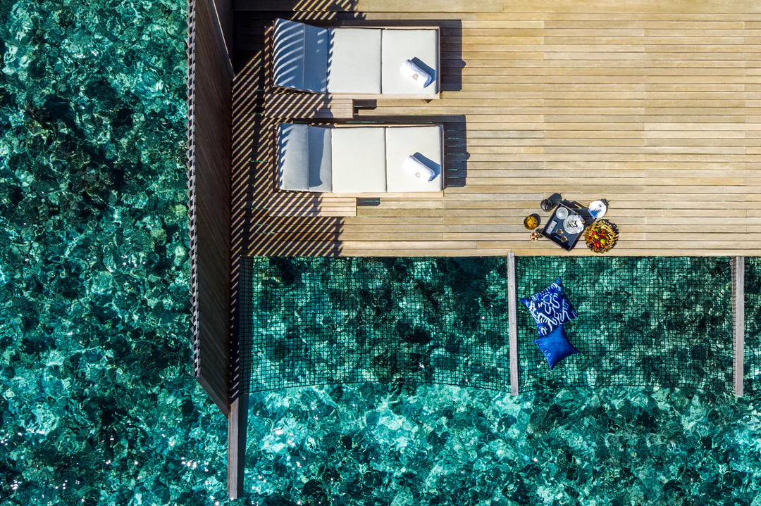 The St. Regis Maldives Vommuli, Dhaalu Atoll — Overhead aerial of two overwater decks and their pools, a snorkeller in the reef below
