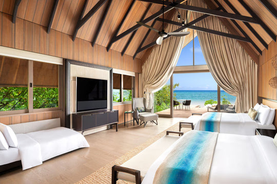 The St. Regis Maldives Vommuli, Dhaalu Atoll — Twin-bedded room under a vaulted timber ceiling, with sliding glass onto the deck