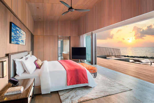 The St. Regis Maldives Vommuli, Dhaalu Atoll — Bedroom at sunset, glass doors open to the deck and an orange sky